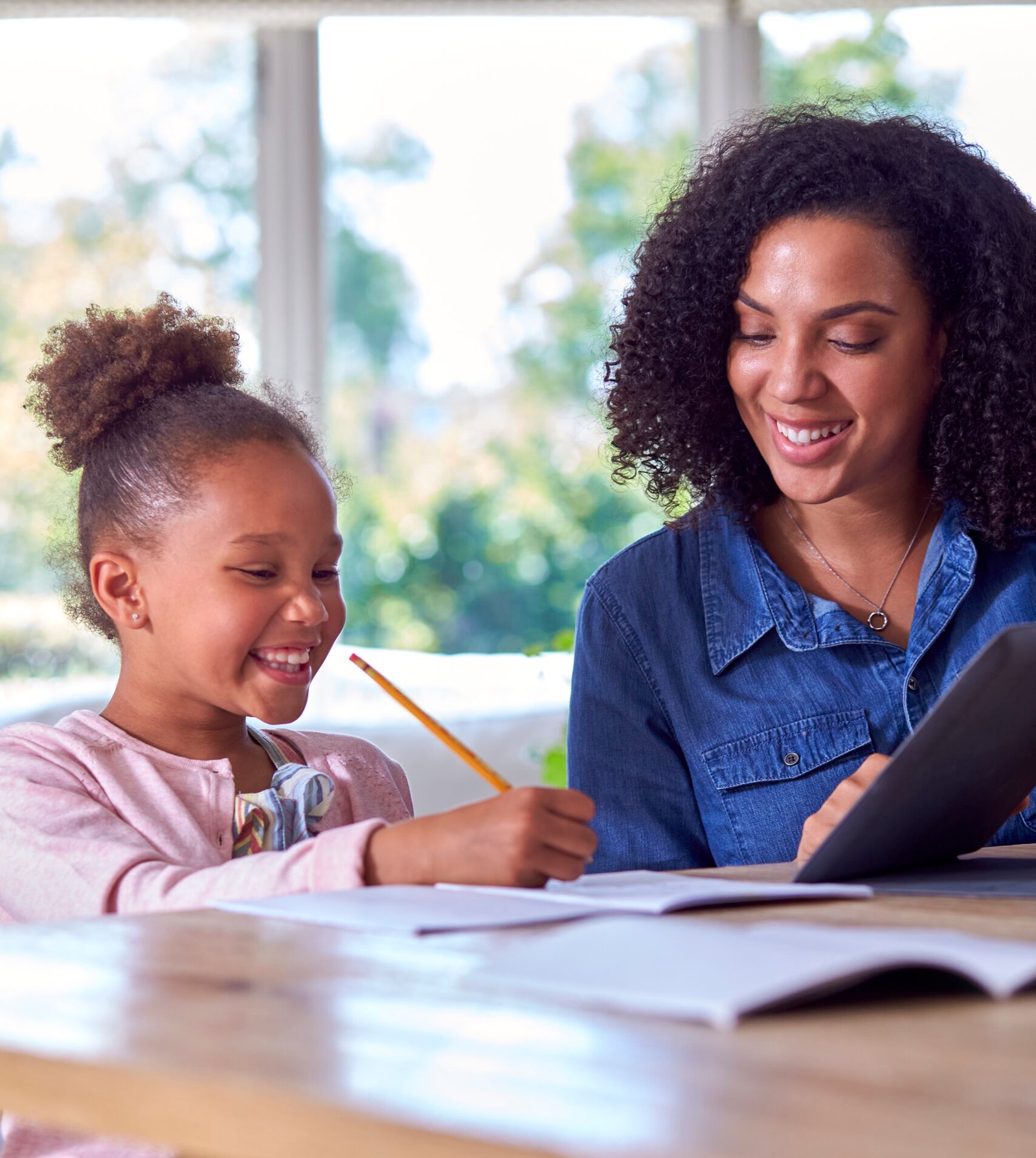 Mother Helping Daughter With Home Schooling Sitting At Table With Digital Tablet